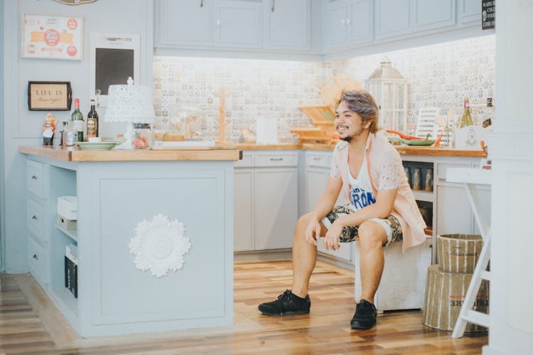 Smiling Young Man Sitting On A Pouffe In The Kitchen