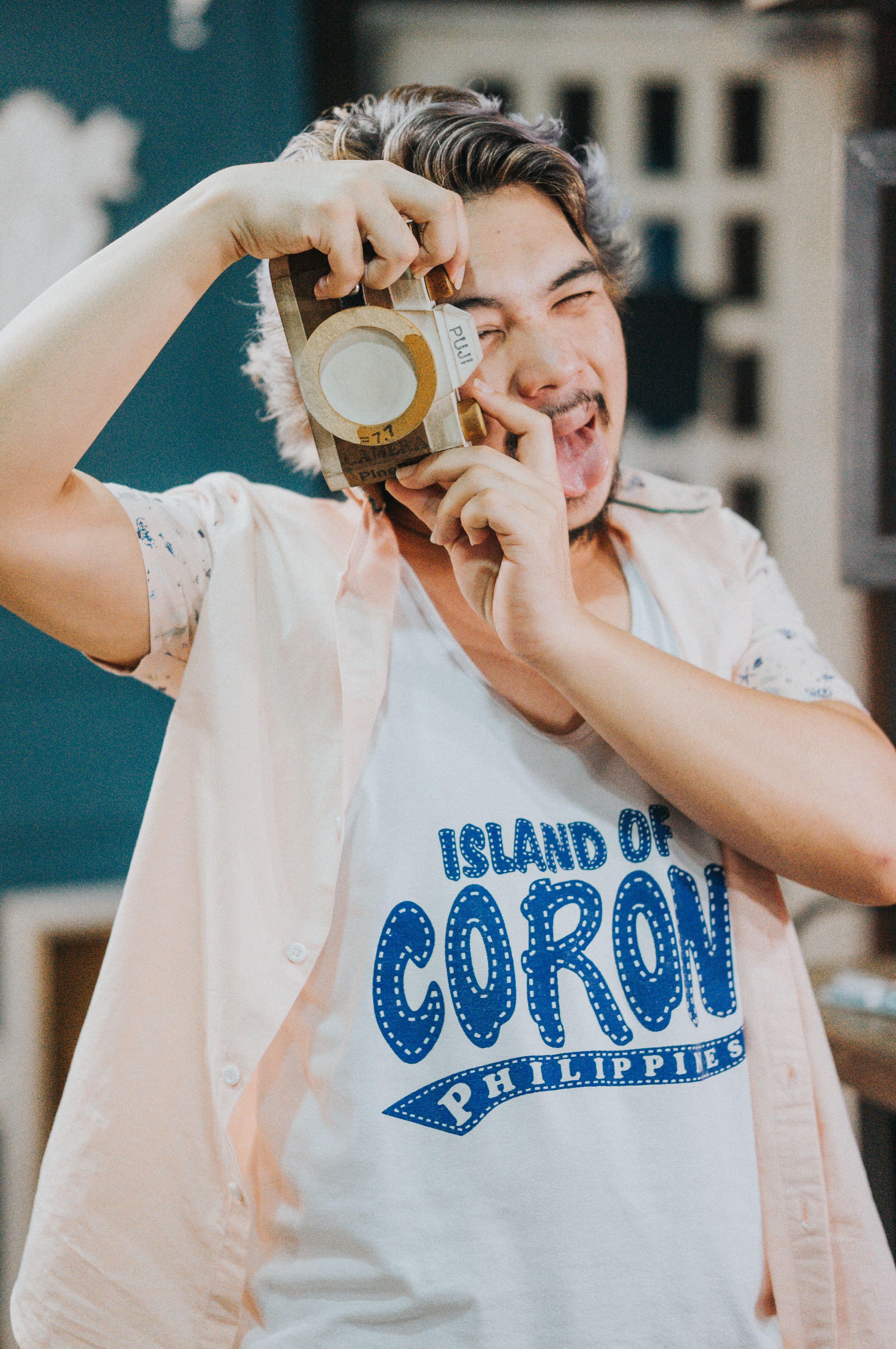 Young man in a 'Coron, Philippines' t-shirt poses humorously with a camera mockup.