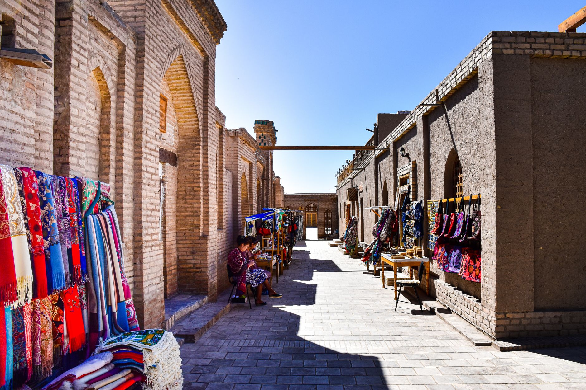 Explore the vibrant bazaar alley lined with textiles in Bukhara's old town marketplace.