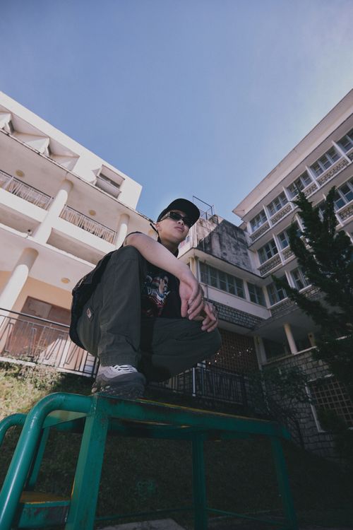 Free A man in urban fashion poses on a bench against a building backdrop. Stock Photo
