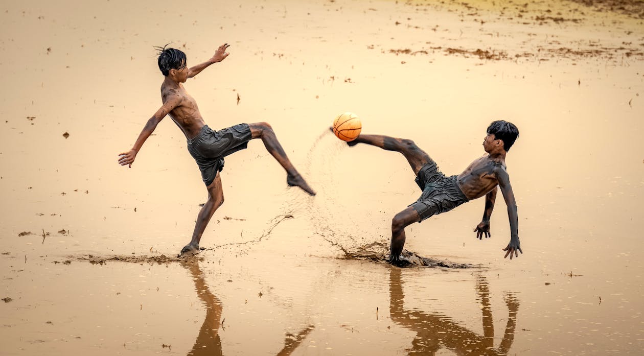 Boys Kicking a Ball in a Muddy Field