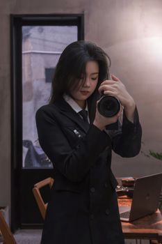 Asian woman in black attire photographing indoors, exuding elegance and focus.