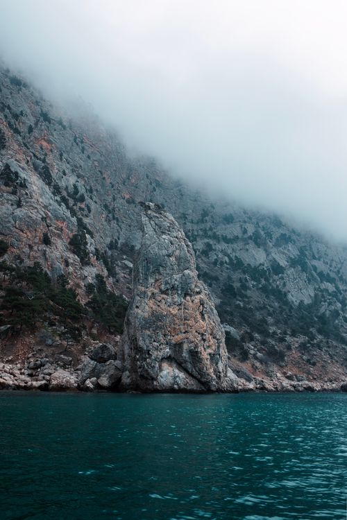 Free A captivating mist-covered rocky cliff rising from the sea, creating a serene coastal scene. Stock Photo