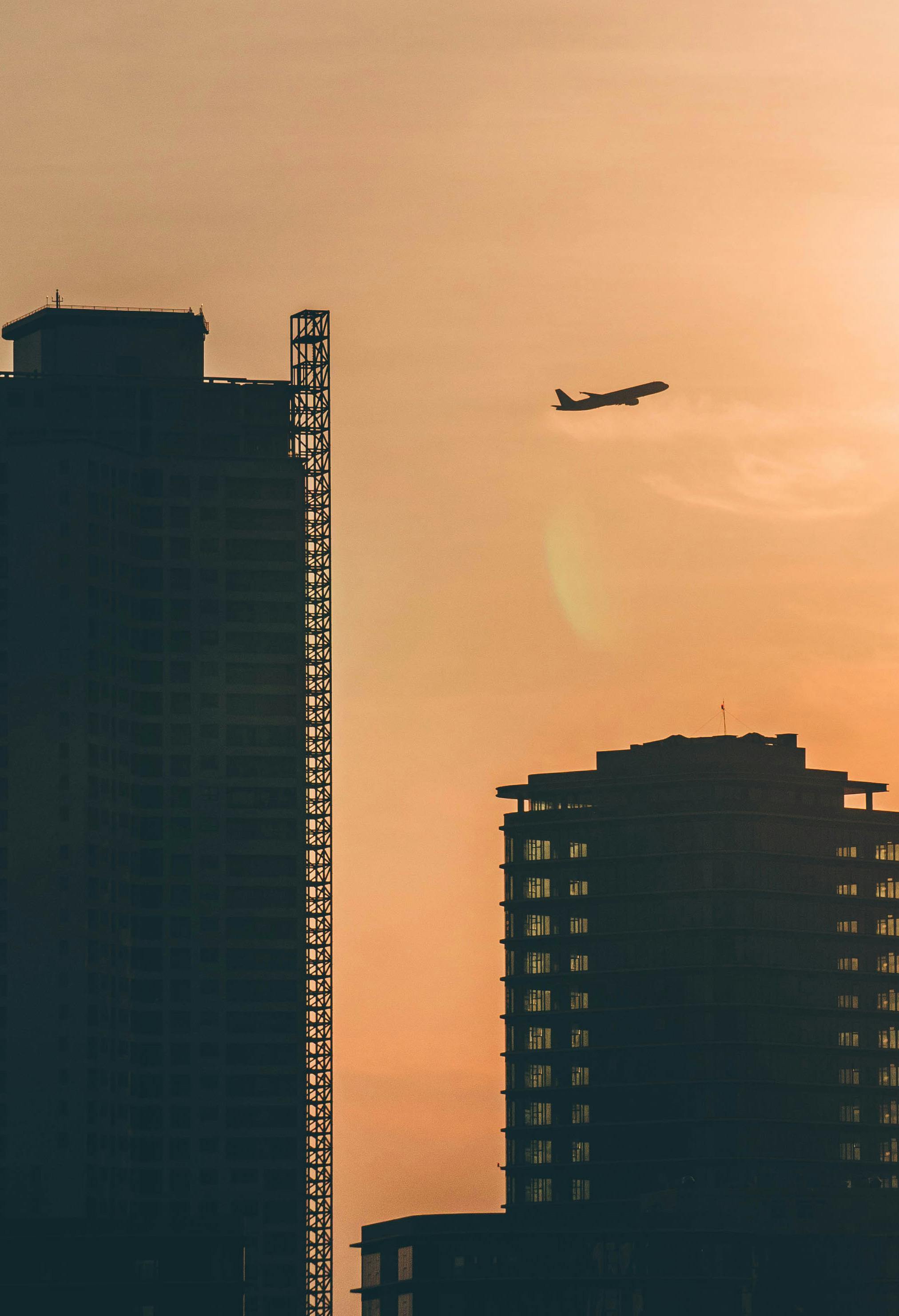 Silhouette of an airplane flying over Đà Nẵng skyscrapers during sunset, capturing urban tranquility.