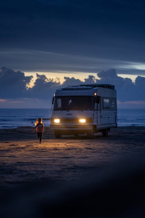 A Child Running on the Beach in front of a Parked Camper Van 