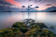 五颜六色的暮色天空下，宁静的景观与苔藓岩石和平静的水域相映成趣