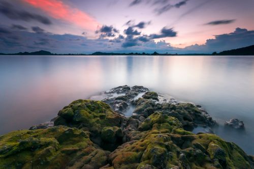 Free Serene landscape with mossy rocks and calm waters under colorful twilight sky. Stock Photo