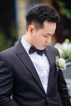 A groom in a black suit with a floral boutonniere, preparing for a wedding ceremony.