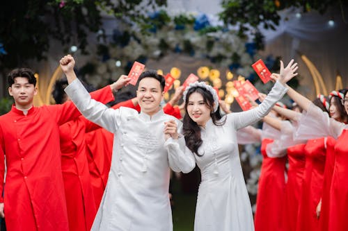 Newlywed in Traditional Vietnamese White Ao Dai Among Wedding Guests in Red Tunics