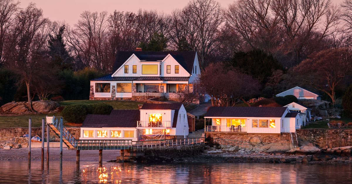 A serene lakeside house illuminated at sunset, reflecting warm lights on the calm water.