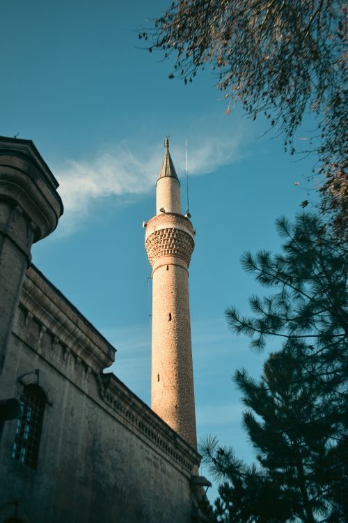 Free A tall minaret of a mosque with trees surrounding under a bright blue sky. Stock Photo