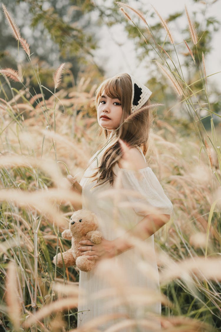 A Girl Holding A Teddy Bear Standing On A Grass Field 