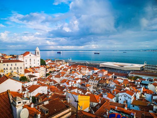 Free Captivating aerial view of Lisbon's historic rooftops by the scenic coastal shore. Stock Photo