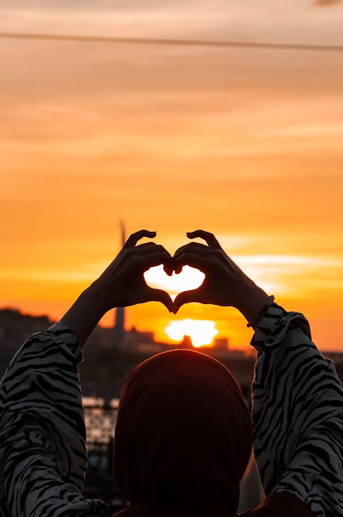 Woman in Hijab Making Heart Shape with Hands at Sunset