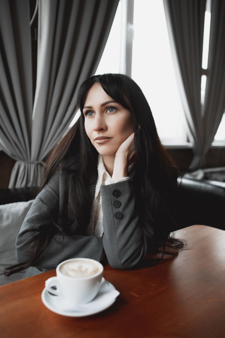 A thoughtful woman sitting in a cafe with a cup of coffee on a wooden table.