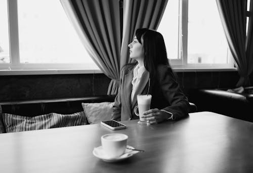 Woman in Jacket Sitting by Table in Black and White