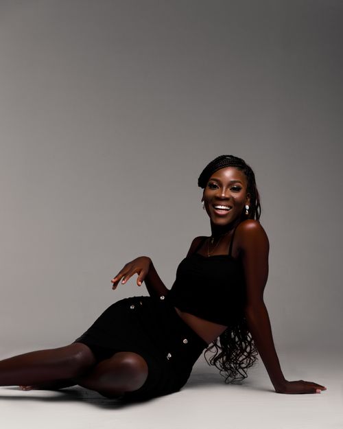 Free Stylish woman in black attire posing elegantly on a gray background with a vibrant smile. Stock Photo