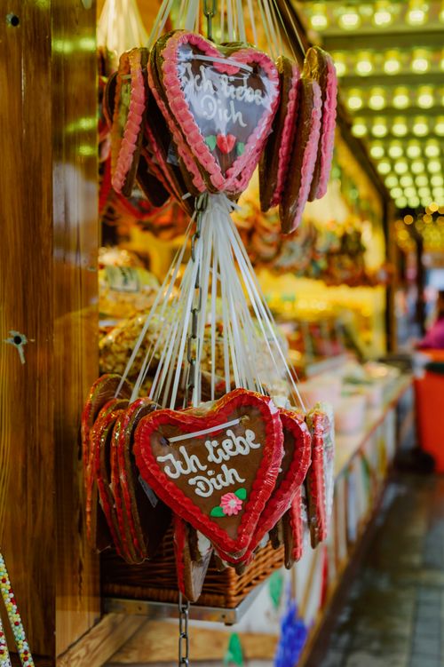Free Close-up of gingerbread hearts with German text at a vibrant market stall, showcasing holiday festivity. Stock Photo