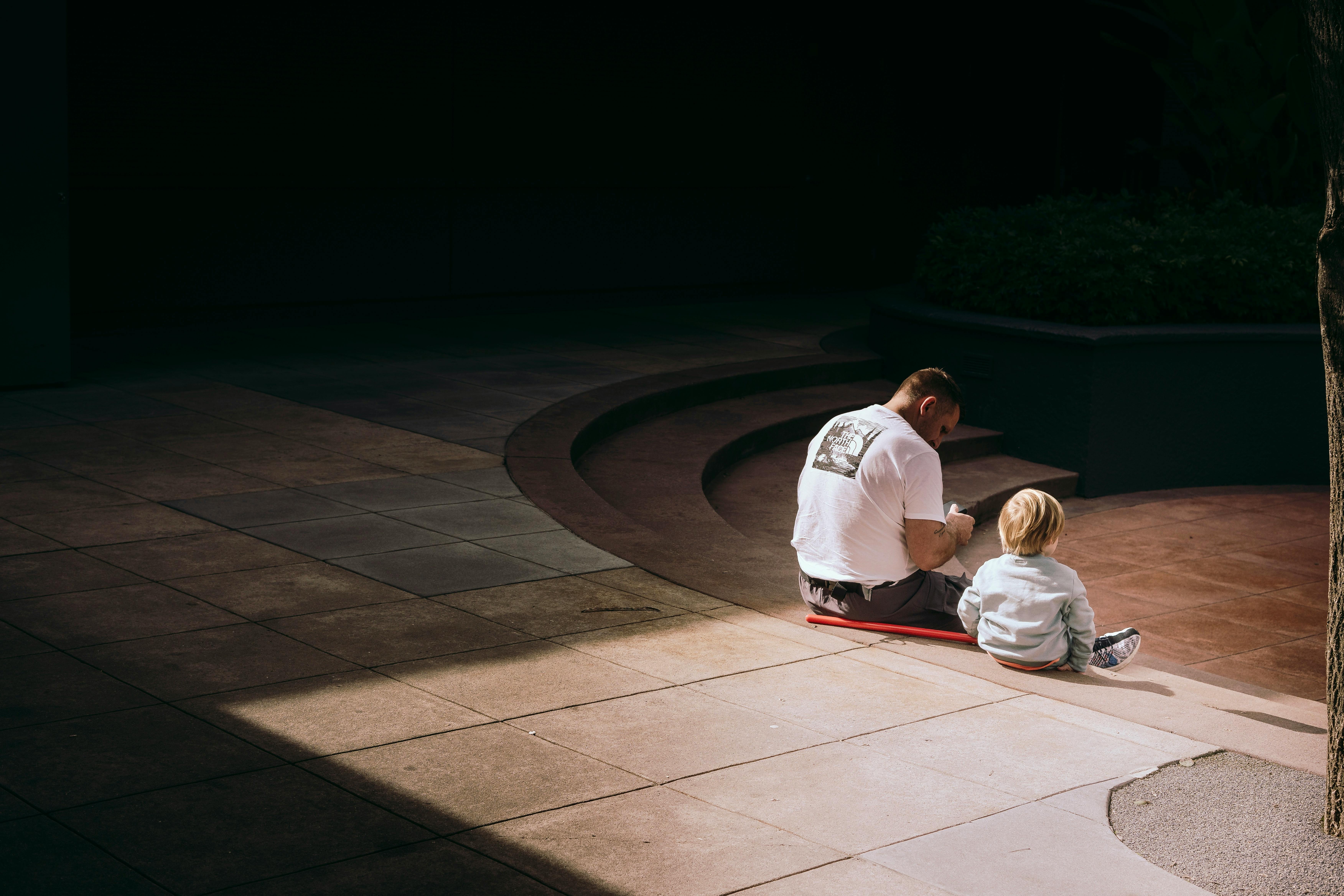 Father and son bonding outdoors, sitting on urban steps in the sunlight.