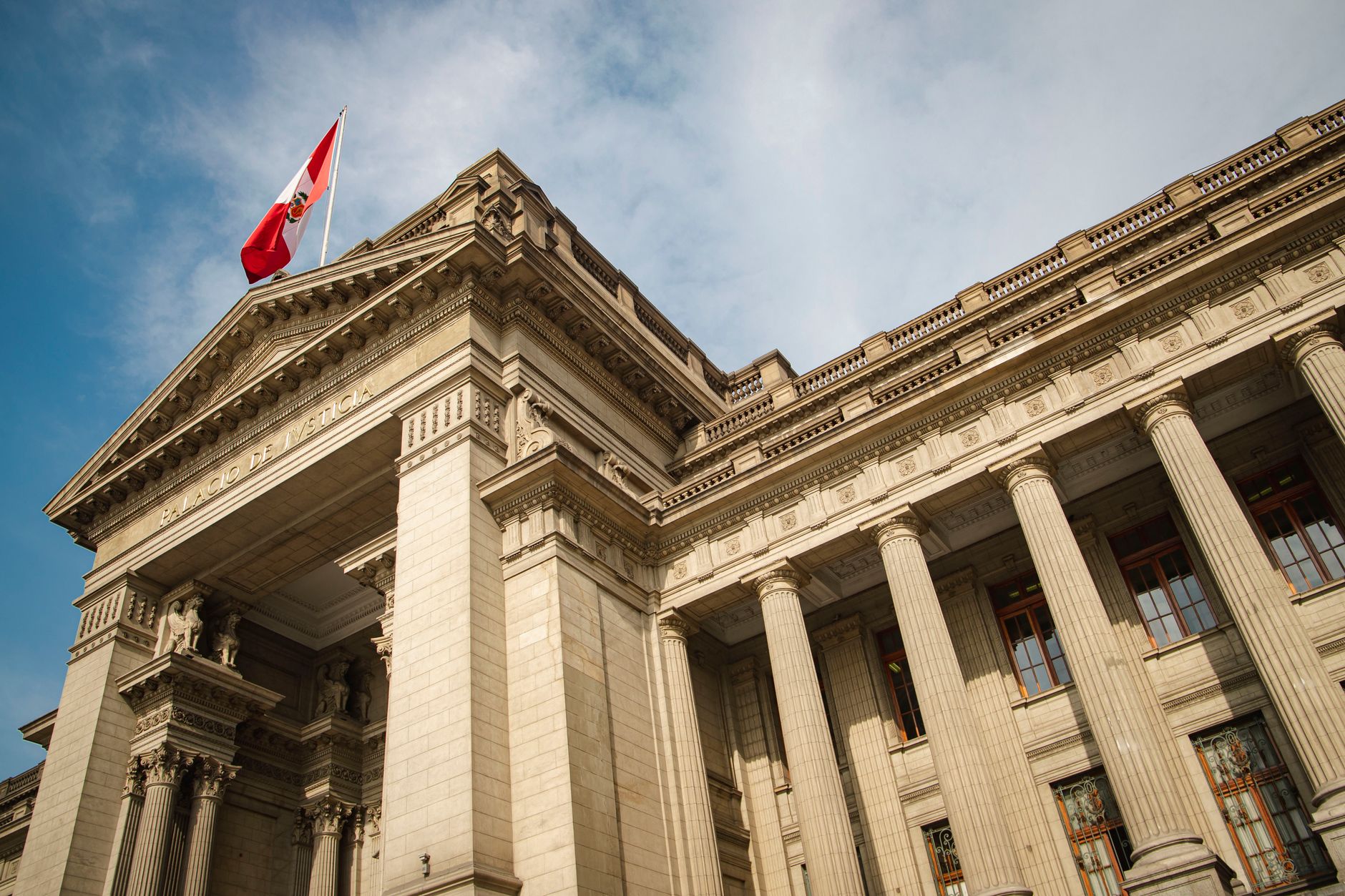 Grand neoclassical government building with Peruvian flag in Lima, Peru, under blue sky.