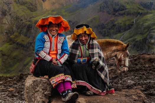 Two women in traditional Andean clothing sit on a rock in the Peruvian mountains, accompanied by a horse.