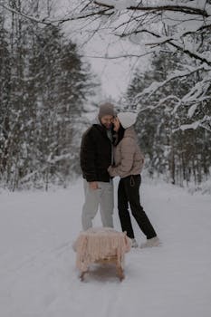 A couple enjoys a romantic winter walk through a snowy forest with a sled.