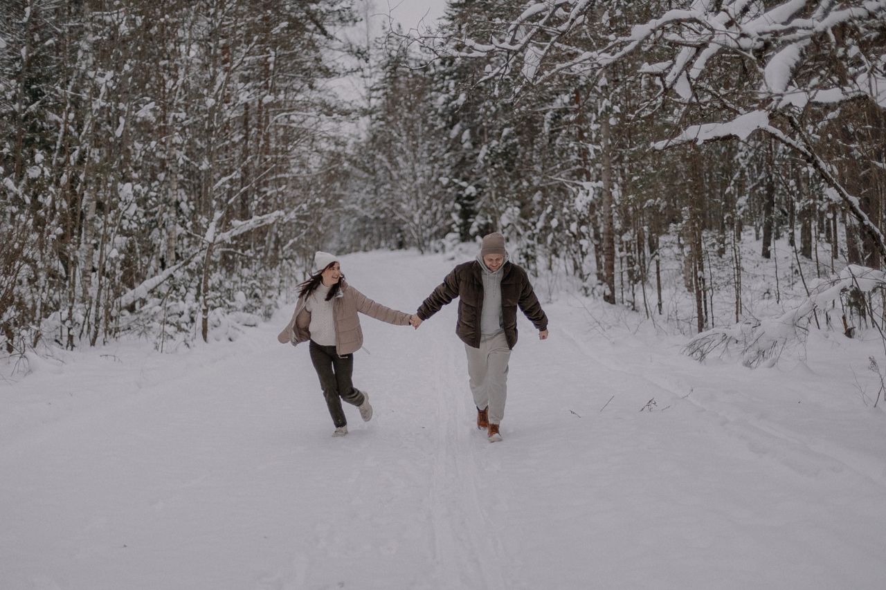 Couple walking hand in hand on a snowy forest path