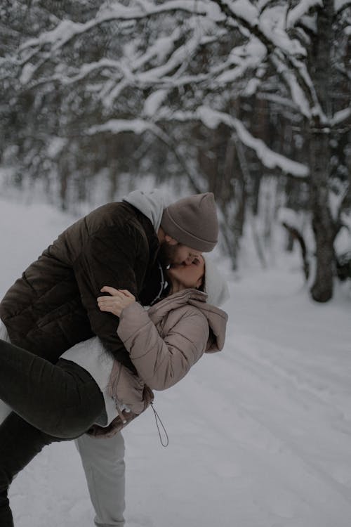 Man Hugging and Kissing Woman in Forest in Winter