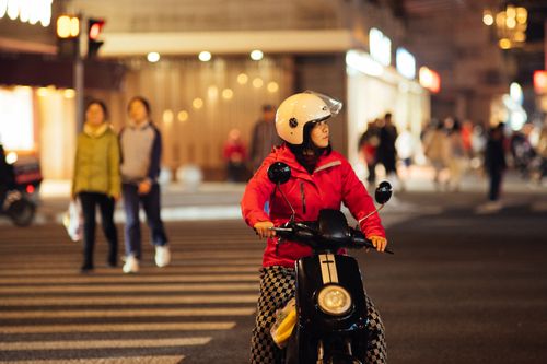 Free Urban night scene with a woman riding a scooter on a busy street, capturing city life. Stock Photo