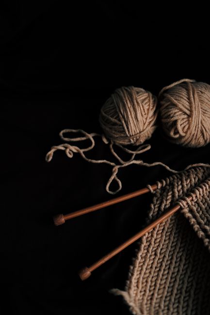 Close-up of yarn balls and knitting needles on a black background, perfect for craft enthusiasts.