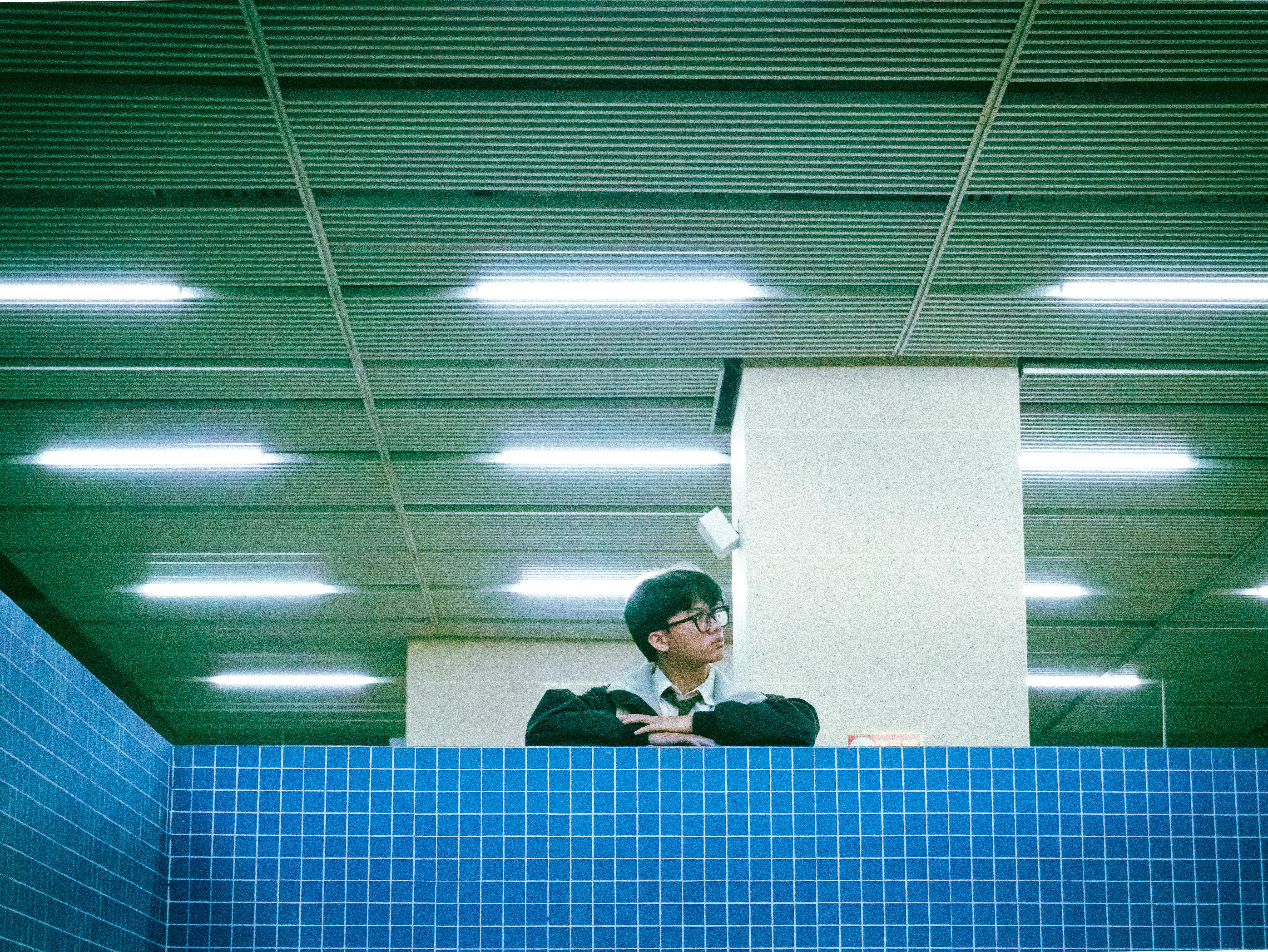 A man stands behind a blue-tiled wall in a subway, looking contemplative.