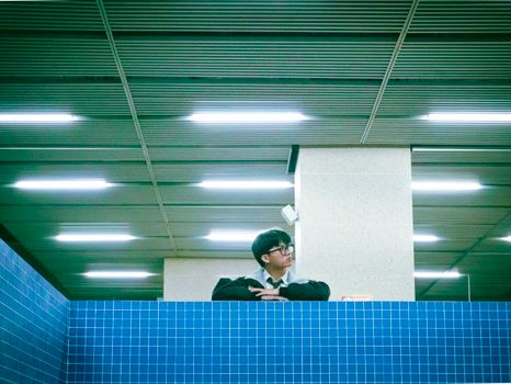A man stands behind a blue-tiled wall in a subway, looking contemplative.