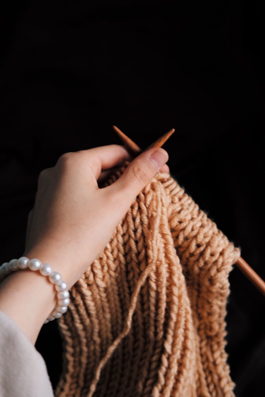 A hand knitting with wooden needles on a black background. Perfect for craft and hobby themes.