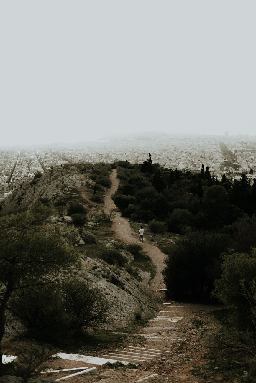 A dirt path winds through rocky terrain, offering a majestic view of the city skyline.