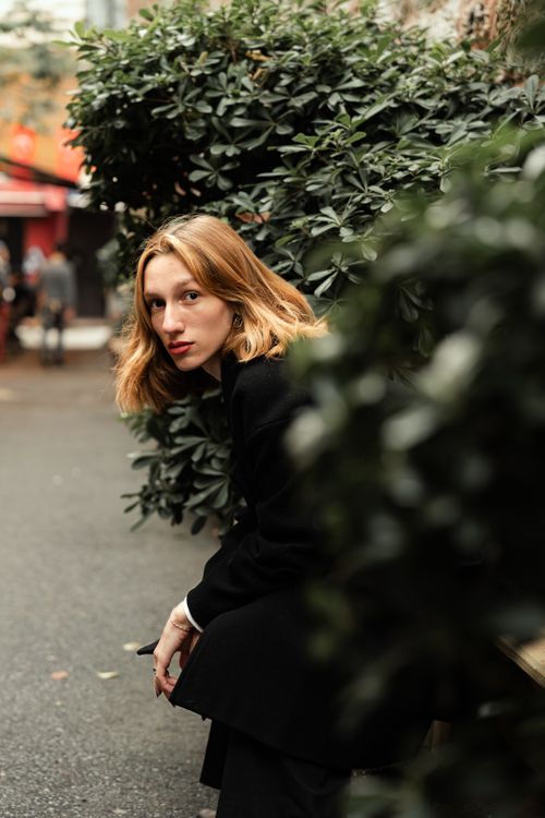 Free A woman in autumn attire poses on a bench surrounded by greenery in a park setting. Stock Photo
