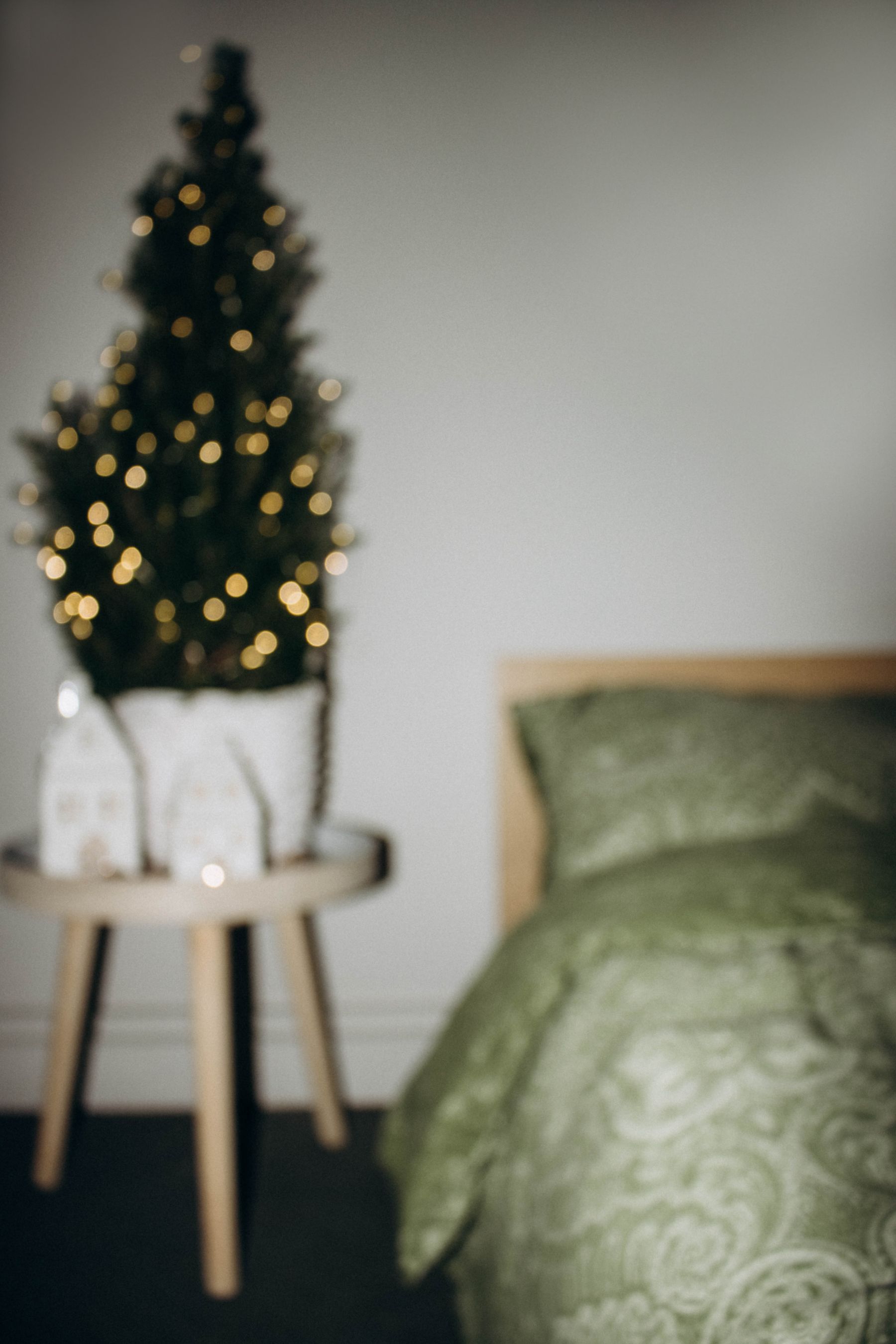 Small lit Christmas tree beside a bed in a compact bedroom