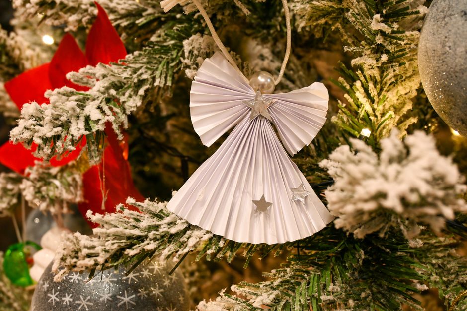 Elegant paper angel ornament hanging on a snow-dusted Christmas tree branch, creating a festive atmosphere.