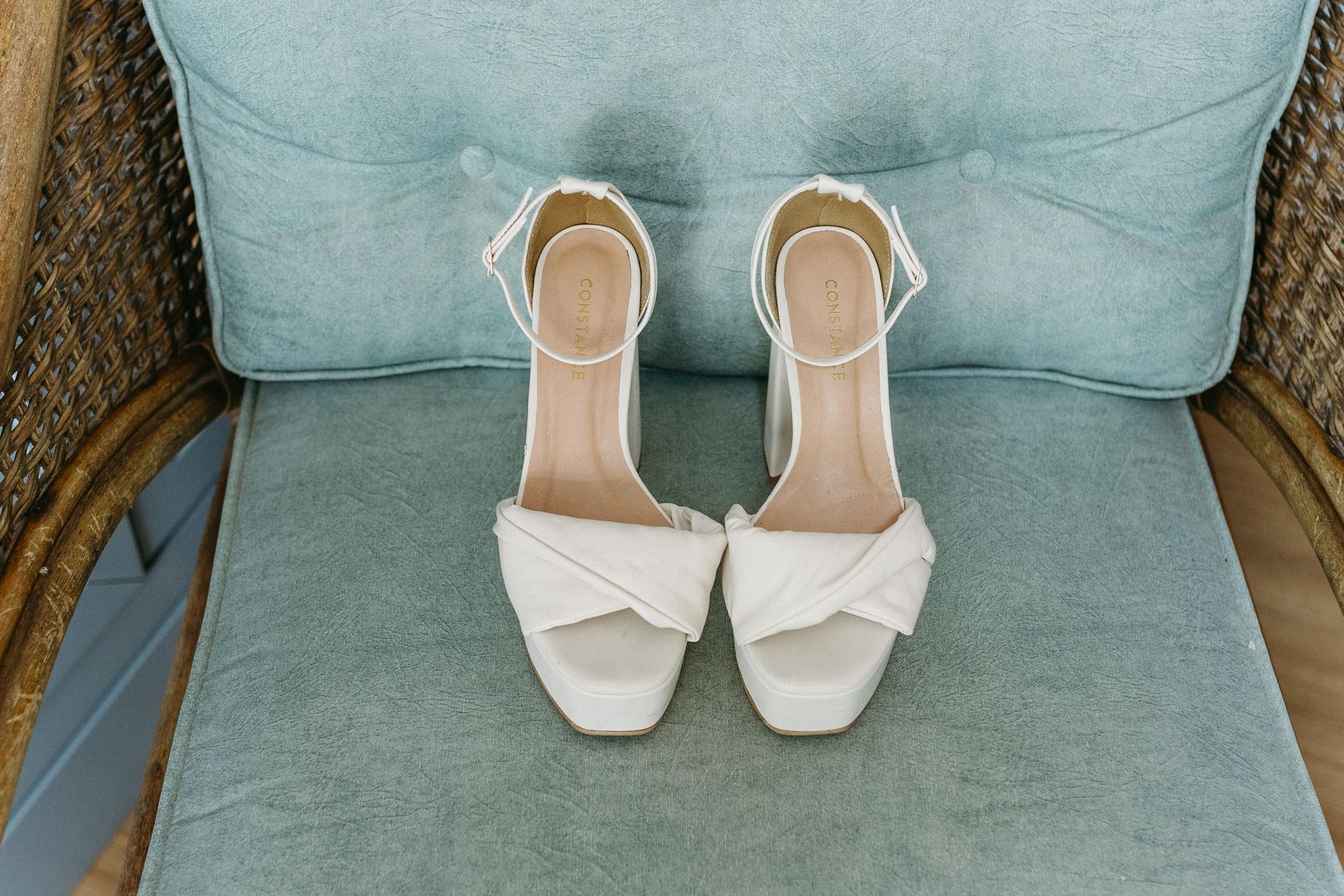 Elegant white high-heeled shoes placed on a cushioned wicker chair, perfect for fashion photography.