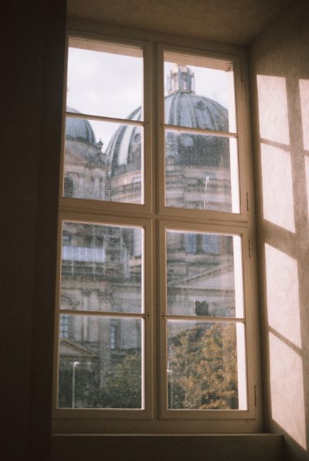 Sunlit view through a window showing the Berlin Cathedral's domes under a clear sky.