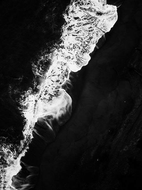 Free Aerial black and white view showcasing dramatic ocean waves crashing on the shore. Stock Photo