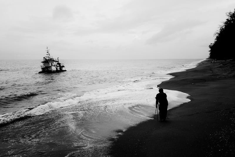 A dramatic black and white scene of a man’s silhouette on Chukai Beach, Malaysia, with a boat in the sea.