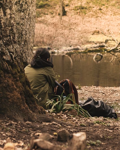 Free A teenage girl sits near a serene pond in a park, surrounded by nature's tranquility. Stock Photo