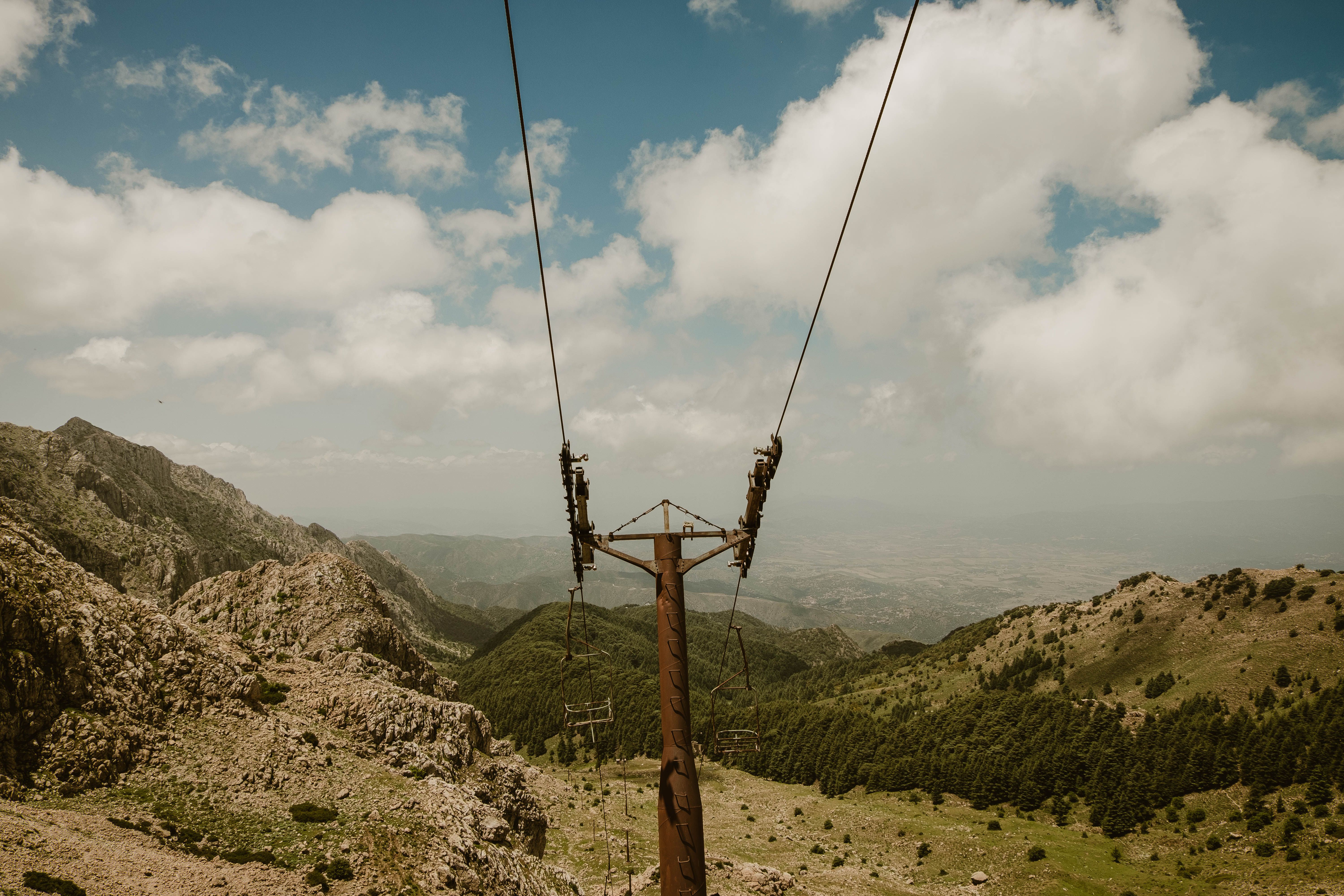 Abandoned ski lift amidst rocky mountains under a bright summer sky, capturing raw natural beauty.