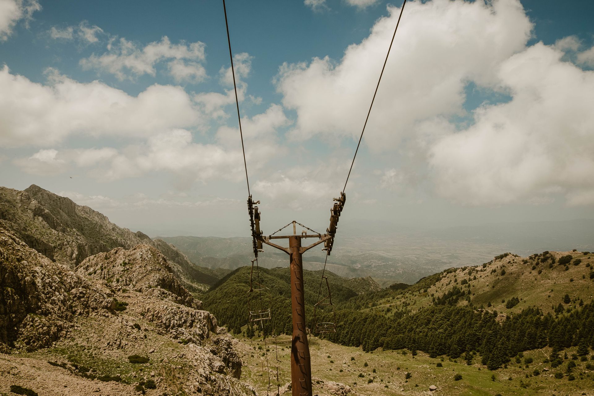 Abandoned ski lift amidst rocky mountains under a bright summer sky, capturing raw natural beauty.