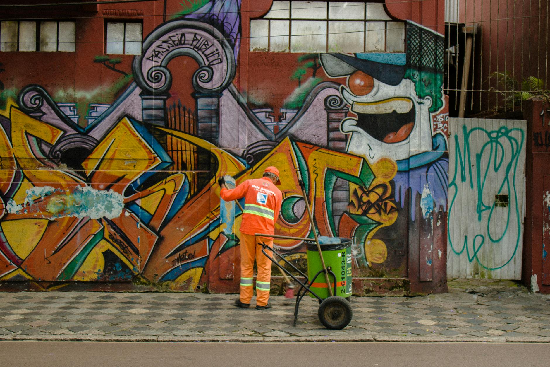 A Man Cleaning the Streets and Standing on the Sidewalk in front of a Graffiti Wall