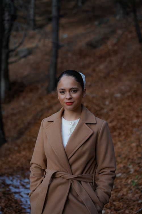Free Woman posing in a brown trench coat amidst a serene autumn forest scene. Stock Photo