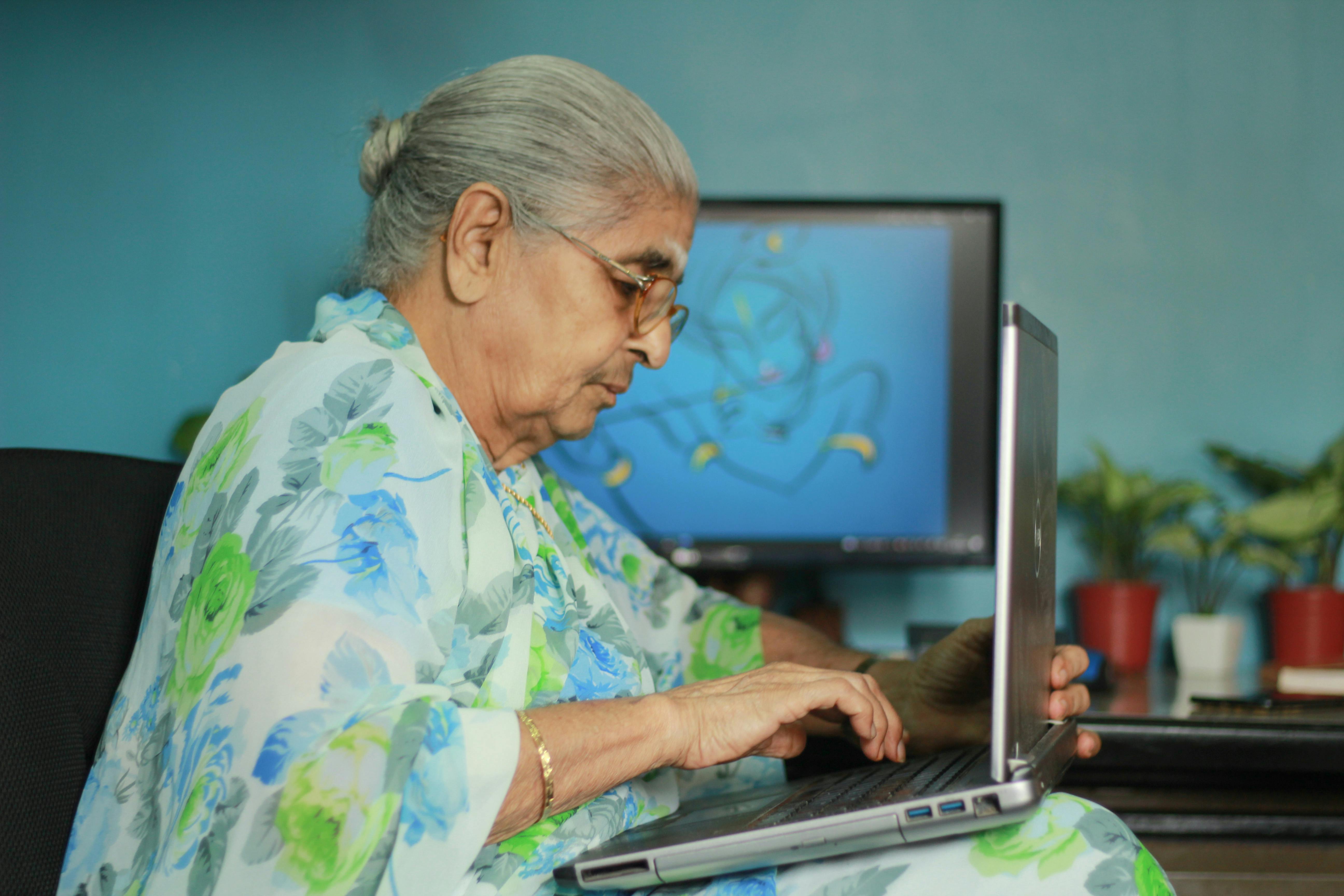 profile of a senior woman wearing a floral blouse using laptop