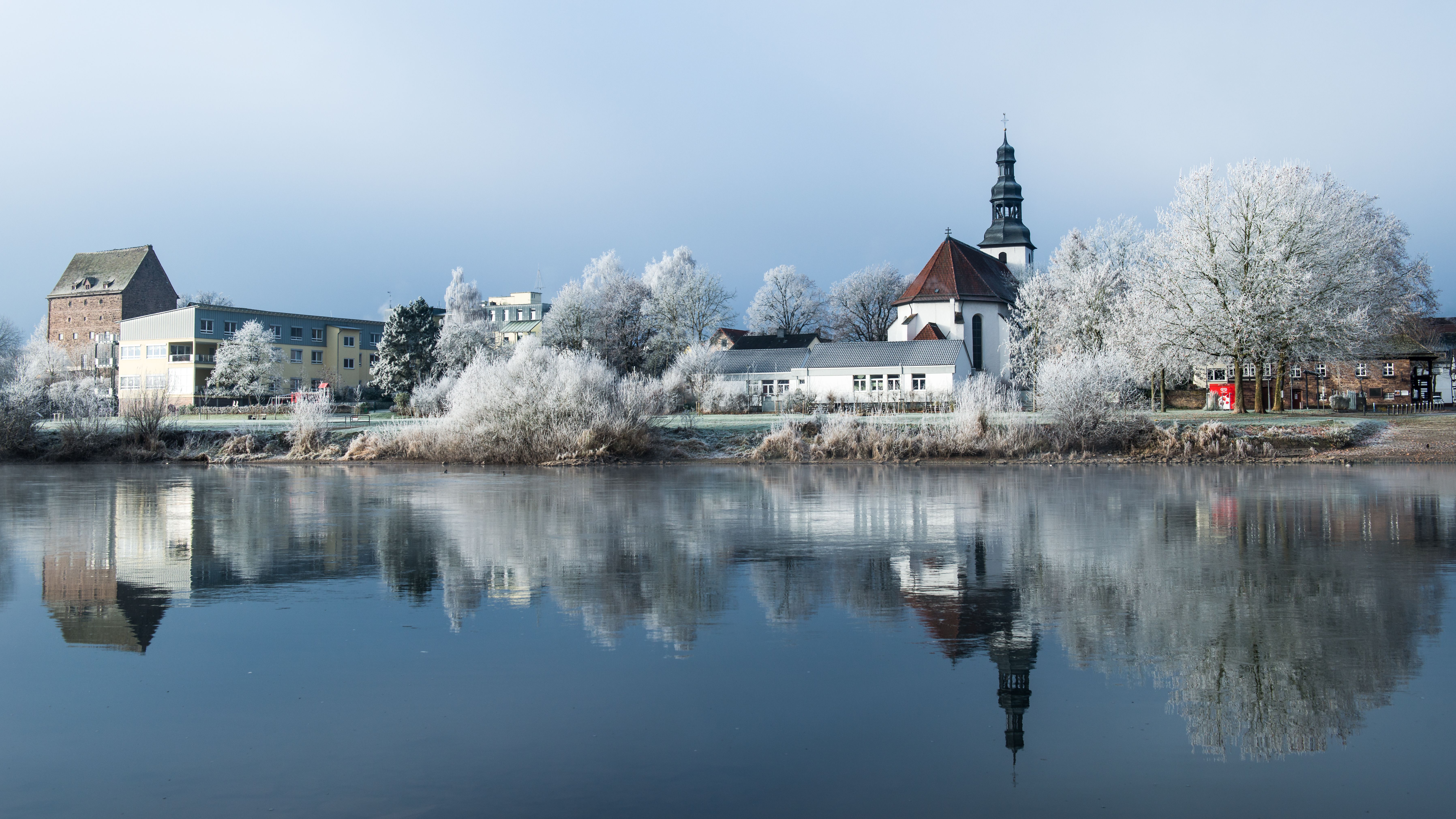 Peaceful winter view of Beverungen, Germany with a church and lake reflection.