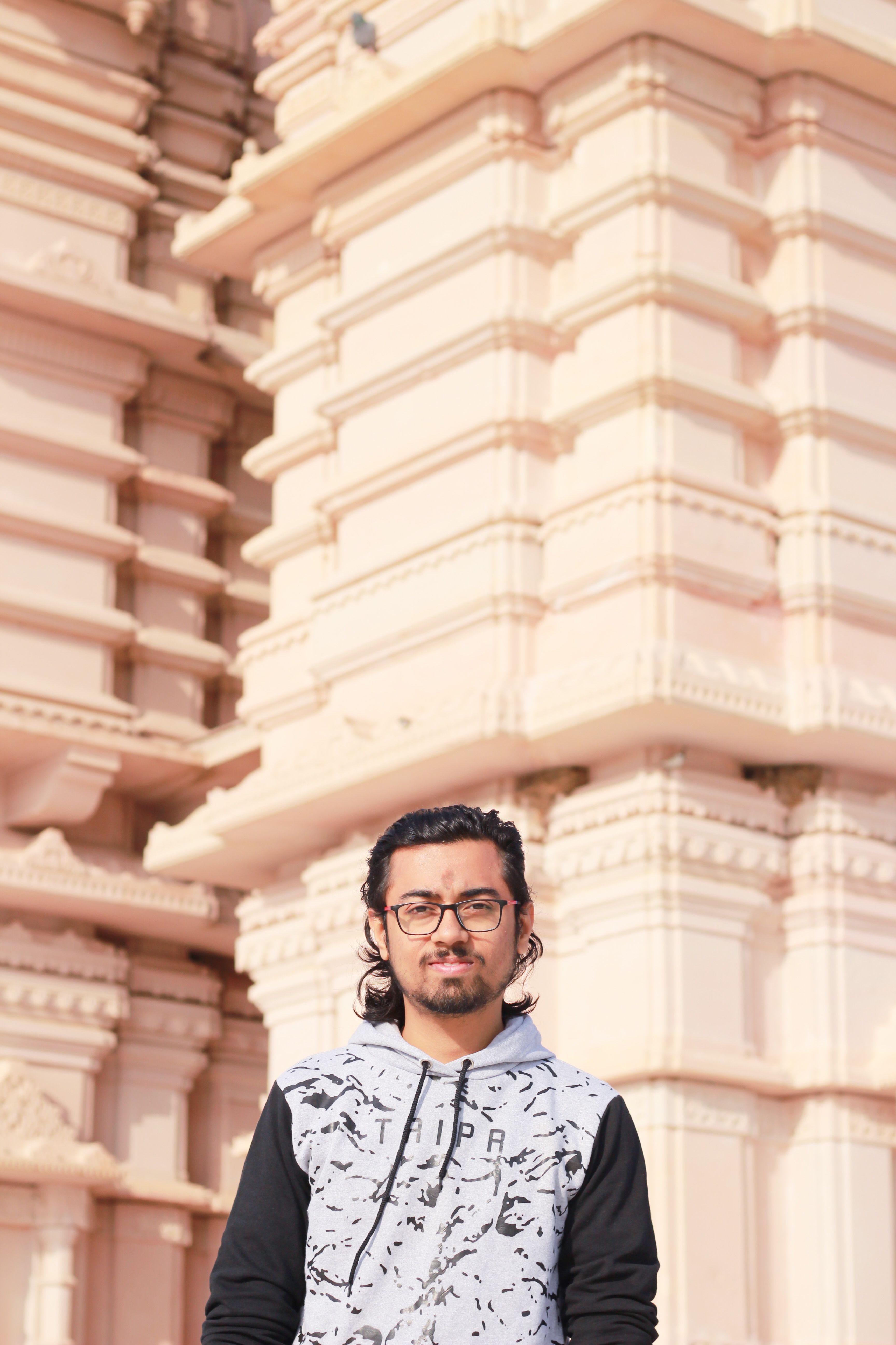 Young man posing confidently in front of beautifully detailed Indian temple architecture, showcasing cultural richness.