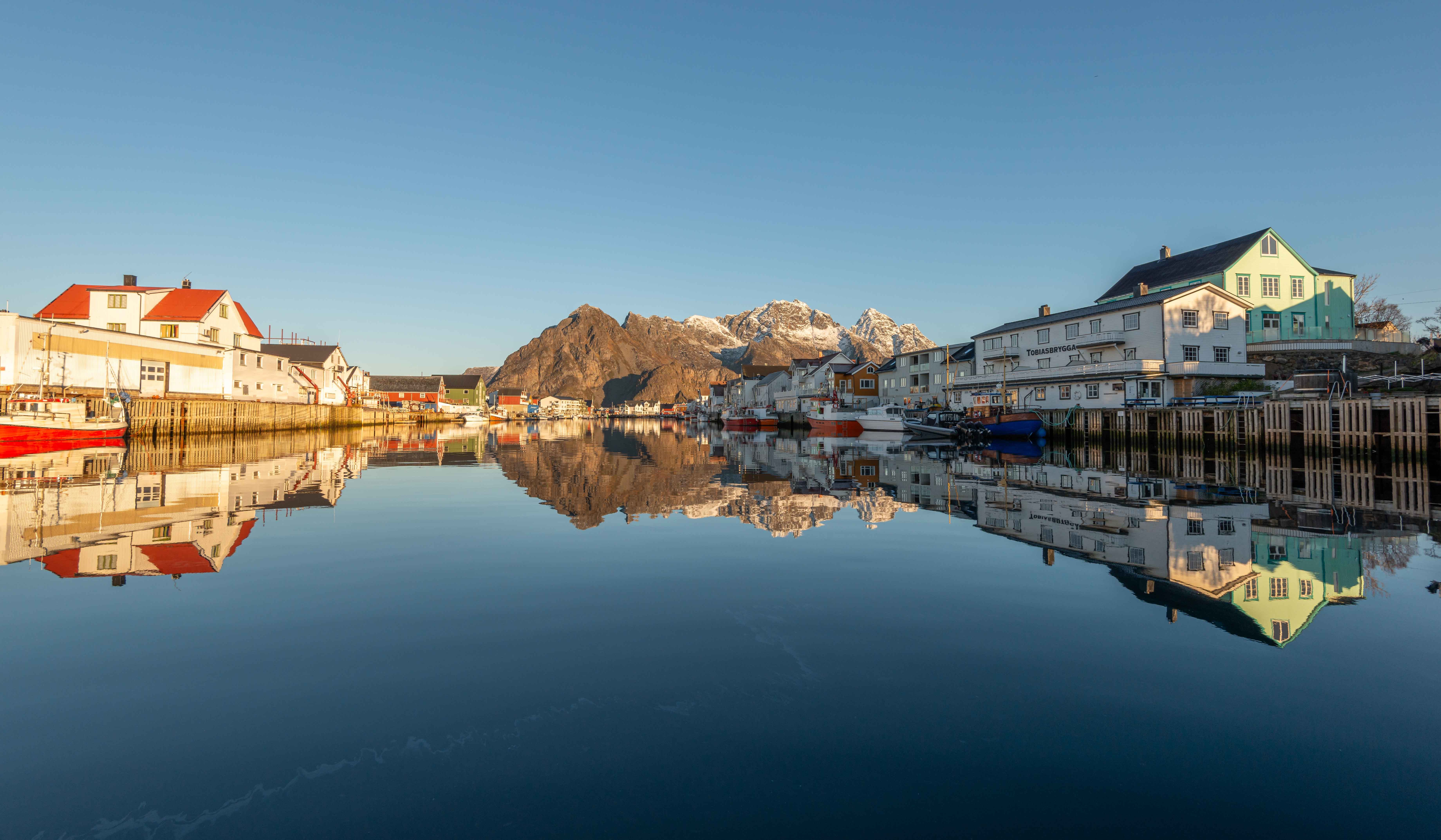 Desa nelayan Henningsvaer di Lofoten, Norwegia, rumah kayu di tepi air dengan pegunungan bersalju di kejauhan